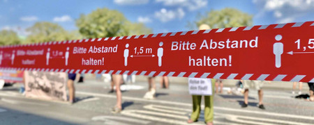 Rotes Absperrband bei Demonstration mit Hinweis "Bitte Abstand halten"  - Link auf: Kommunen gegen globale Krisen