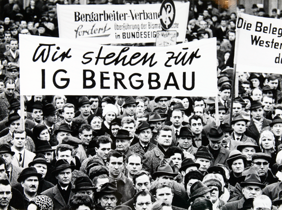 Zu sehen ist eine historische Aufnahme eines Aufstands in der Krise des Bergbaus. Hochgehalten wird ein Banner mit dem Satz "Wir stehen zur IG BERGBAU".