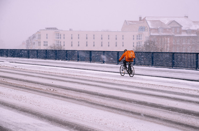 Ein einsamer Lieferkurier fährt über eine mit Schnee bedeckte Schnellstraße mit dem Fahrrad