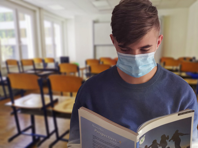 Schüler mit Maske liest ein Buch in Klassenzimmer