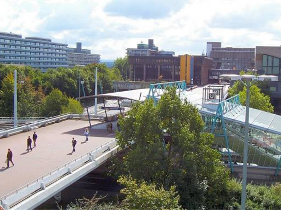 Blick auf das Universitätsgebäude der Uni Bochum, im Vordergrund ist eine Brücke mit vielen Fußgängern drauf 