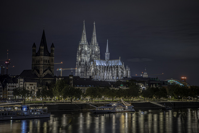 Kölner Dom, hell erleuchtet, vor der Rheinkulisse bei Nacht