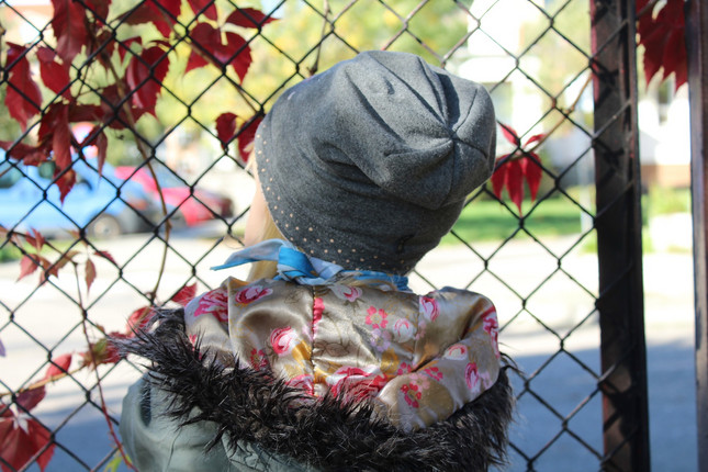 Rückansicht Kind mit Mütze vor Zaun