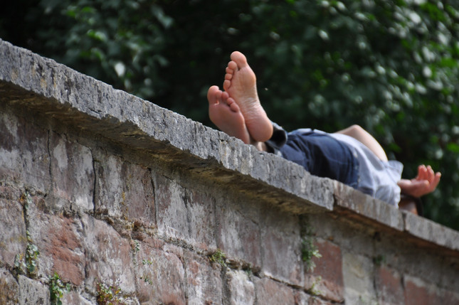Mensch mit nackten Füßen liegt auf einer Mauer