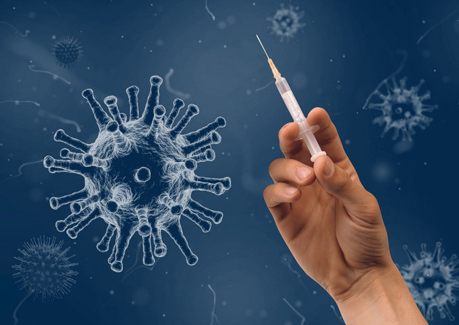 Eine Hand hält eine Spritze für eine COVID-19-Impfung. Im Hintergrund schweben zur Illustration animierte Sars-CoV-2-Viren.