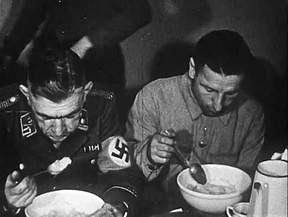 Foto von zwei Personen beim Essen, linke Person mit Hakenkreuz am Arm